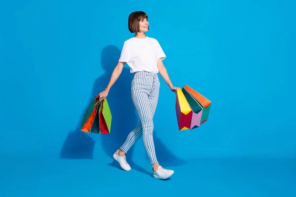 Ganzkörpergröße Foto Mädchen mit Taschen zu Fuß in Einkaufszentrum suchen leeren Raum isoliert lebendige blaue Farbe Hintergrund — Stockfoto