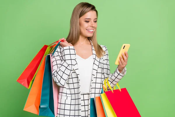 Portrait of attractive cheerful girl carrying bags new clothes using device order isolated over bright green color background — Stock Photo, Image