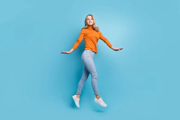 Foto van lieve charmante jonge vrouw gekleed oranje trui glimlachen springen hoog lopen geïsoleerde blauwe kleur achtergrond — Stockfoto