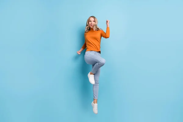 Foto von Glück süße junge Frau gekleidet orange Pullover lächelnd aufsteigende Fäuste isoliert blaue Farbe Hintergrund — Stockfoto