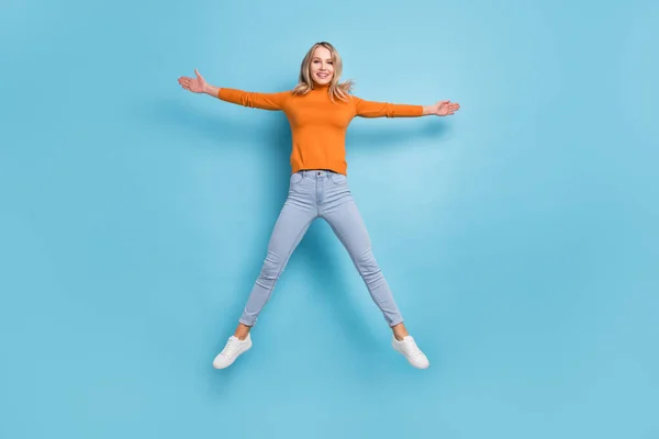 Foto van schattige jonge dame dragen oranje trui springen hoog als ster glimlachen geïsoleerde blauwe kleur achtergrond — Stockfoto