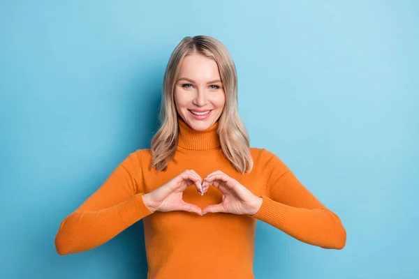 Foto von entzückenden charmante junge Frau gekleidet orange Pullover lächelnd zeigt Finger Herz isoliert blaue Farbe Hintergrund — Stockfoto