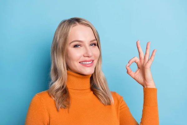 Foto de mujer joven bastante adorable vestido suéter naranja sonriendo mostrando signo okey aislado fondo de color azul — Foto de Stock