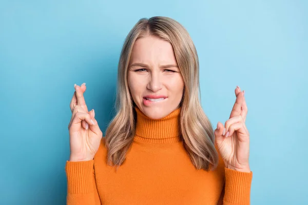 Foto av tveksam osäker ung dam bära orange tröja bita läpp fingrar korsade isolerad blå färg bakgrund — Stockfoto