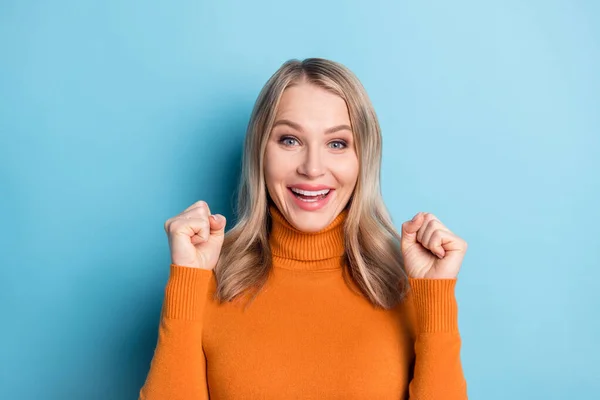 Foto de bonito sorte jovem senhora desgaste laranja suéter sorrindo levantando punhos isolado azul cor fundo — Fotografia de Stock