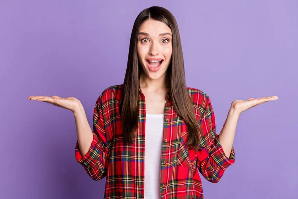 Foto van koele hoera brunette kapsel jonge dame houden lege ruimte dragen rood geruite shirt geïsoleerd op paarse kleur achtergrond — Stockfoto