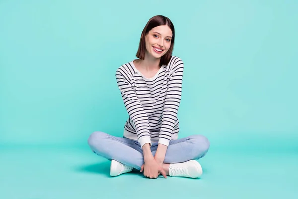 Foto de calma adorável senhora sentar chão brilhante sorriso usar camisa listrada isolado no fundo cor teal — Fotografia de Stock