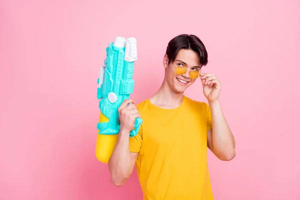 Fotografie mladého pohledného chlapa šťastný pozitivní úsměv držet vodní pistole dovolená vypadat prázdný prostor izolované přes růžové barvy pozadí — Stock fotografie
