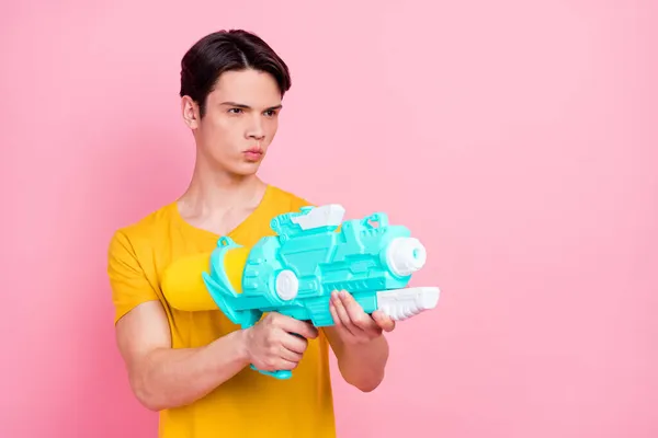 Fotografie soustředěného chlapa držet vodní pistole cíl prázdný prostor nosit žluté tričko izolované na růžovém pozadí — Stock fotografie