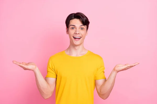 Foto de animada promotor cara mãos segurar objetos de espaço vazio boca aberta desgaste amarelo t-shirt isolado no fundo rosa — Fotografia de Stock