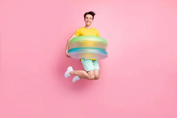 Photo de jeune garçon doux enfantin habillé t-shirt jaune sautant haut à l'intérieur du cercle de natation isolé fond de couleur rose — Photo