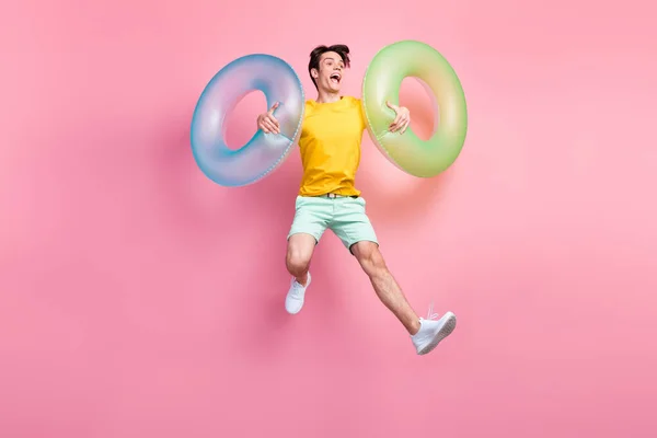 Photo de drôle de positif gars saut porter des cercles gonflables porter jaune t-shirt shorts baskets isolées sur fond rose — Photo