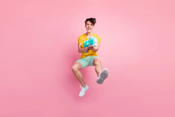 Foto av galen våldsam funky kille hoppa skott pump vatten pistol bära gul t-shirt shorts skor isolerad på rosa bakgrund — Stockfoto