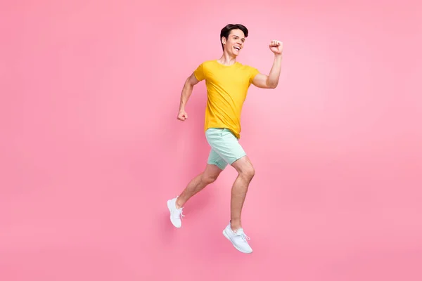 Foto de perfil de chico alegre activo salto rápido prisa prisa llevar camiseta amarilla pantalones cortos calzado aislado sobre fondo rosa —  Fotos de Stock