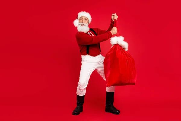 Pleine longueur photo de Santa Claus heureux sourire positif tenir sac présent nouvel an isolé sur fond de couleur rouge — Photo