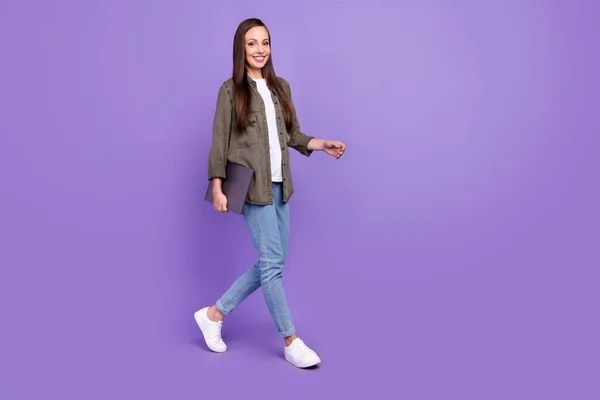 フルサイズプロフィール側の写真の笑顔陽気な女性行く歩くとノートパソコンで隔離された鮮やかな紫色の背景 — ストック写真