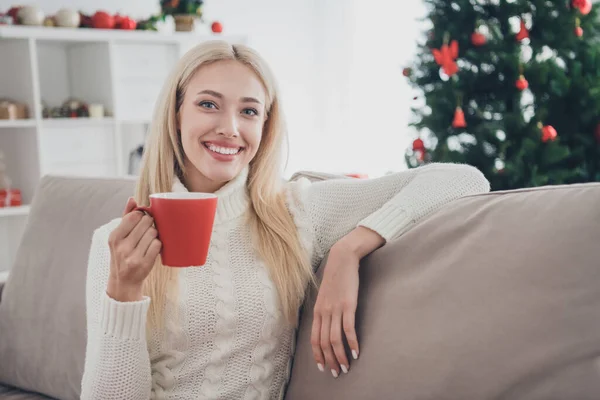Φωτογραφία από χαριτωμένο γοητευτικό νεαρή γυναίκα ντυμένη λευκό πουλόβερ πίνοντας ζεστό τσάι χαμογελώντας σε εσωτερικούς χώρους σπίτι δωμάτιο — Φωτογραφία Αρχείου