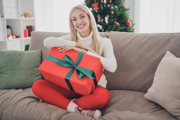 Beyaz kazaklı, vücut ölçülerinde bir kadın. Evdeki koltukta büyük bir hediye kutusu tutuyor. — Stok fotoğraf