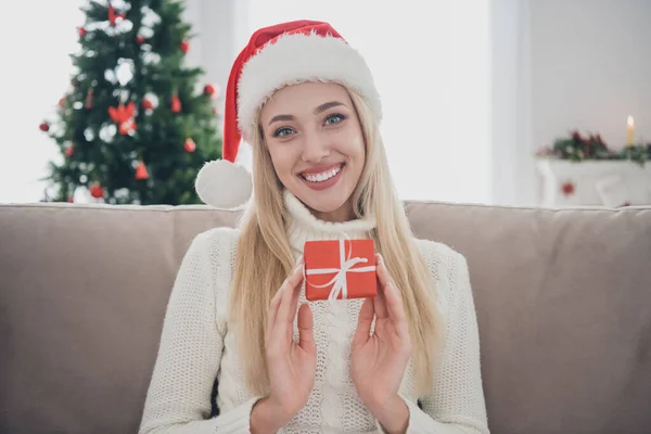 Фото красивої молодої леді носить в'язаний пуловер, посміхаючись тримаючи невелику подарункову коробку в приміщенні домашньої кімнати — стокове фото