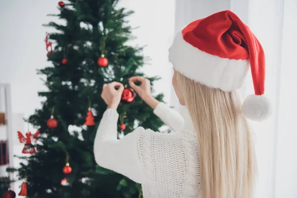 젊고 매력적 인 여성 이 크리스마스 선물로 나무를 장식하고 있는 사진 집 안에서 산타 클로스 모자를 쓰고 집안으로 들어간다. — 스톡 사진