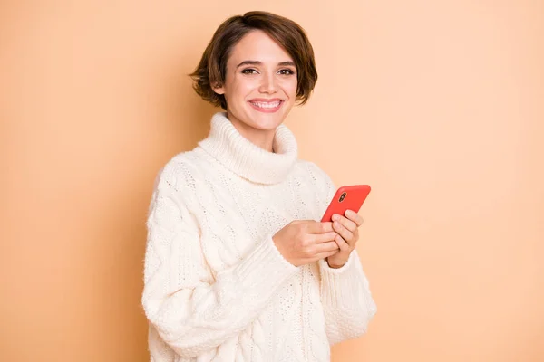 Фотопортрет красивой девушки в свитере с помощью мобильного телефона, улыбающейся изолированно на пастельно-бежевом фоне — стоковое фото
