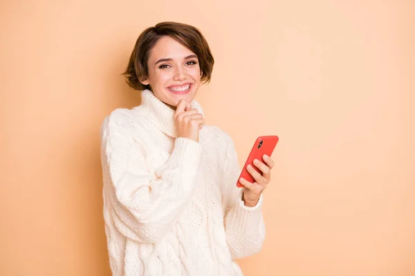 Фото веселой позитивной молодой девушки держать за руку подбородок смартфона думать изолированы на пастельно-бежевом фоне — стоковое фото