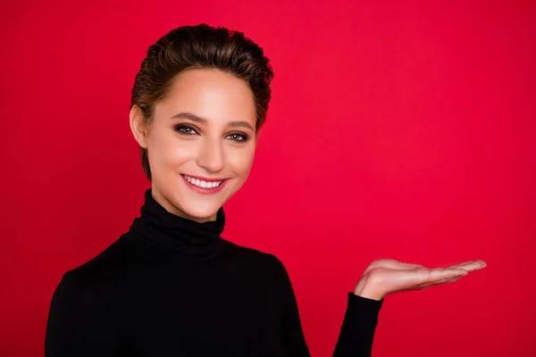 Фото молодой веселой девушки счастливой позитивной улыбкой держать руку продукт промо-предложение предложить изолированы на красном фоне — стоковое фото