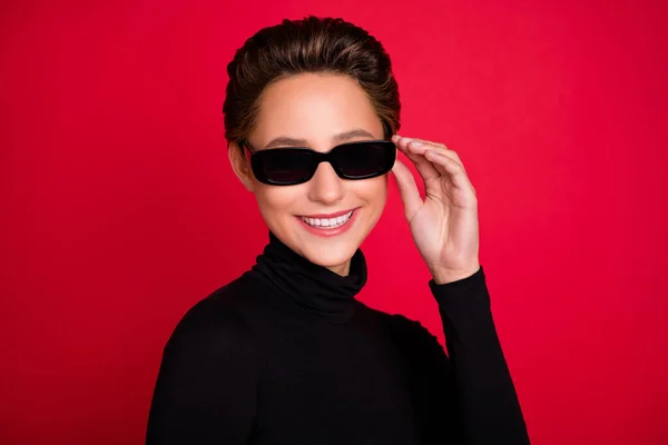 Фото молодой женщины счастливой позитивной улыбкой руки касаются солнцезащитные очки прохладно изолированы на красный цвет фона — стоковое фото