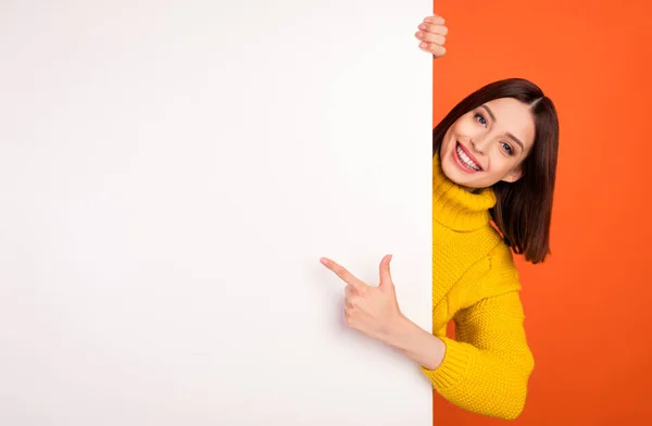 Photo of young woman happy positive smile point finger empty space billboard ad advice choice isolated over orange color background — Stock Photo, Image