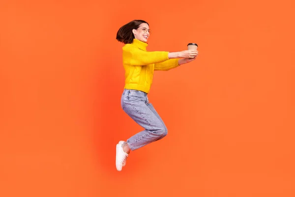 Full tělo profil boční fotografie mladé ženy šťastný pozitivní úsměv dát šálek kávy skok nahoru izolované přes oranžové barvy pozadí — Stock fotografie