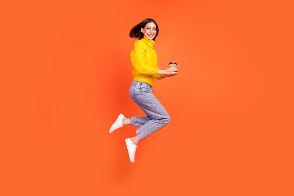 Full length profile side photo of young woman happy positive smile jump takeaway coffee isolated over orange color background — Stock Photo, Image