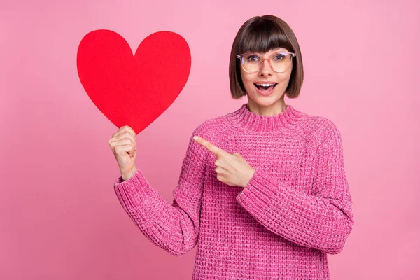 Foto de jovem encantador feliz positivo mulher bonita ponto dedo segurar mão coração forma sorriso isolado no fundo cor-de-rosa — Fotografia de Stock