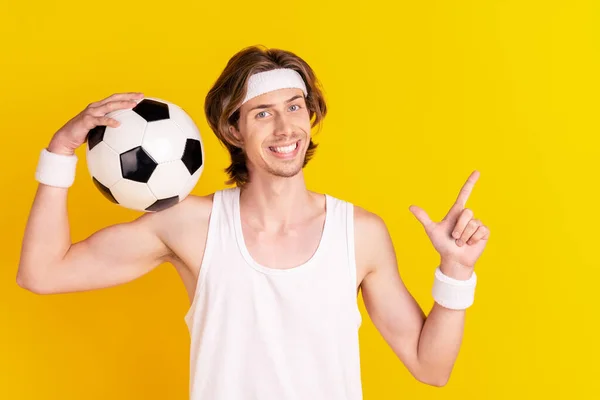 Портрет красивого веселого парня, держащего футбольный мяч, показывающий пространство для копирования, изолированное на ярко-желтом фоне — стоковое фото