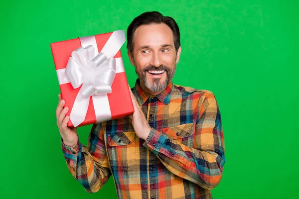 Retrato de homem alegre atraente curioso segurando em mãos giftbox adivinhando o que dentro isolado sobre fundo de cor verde brilhante — Fotografia de Stock