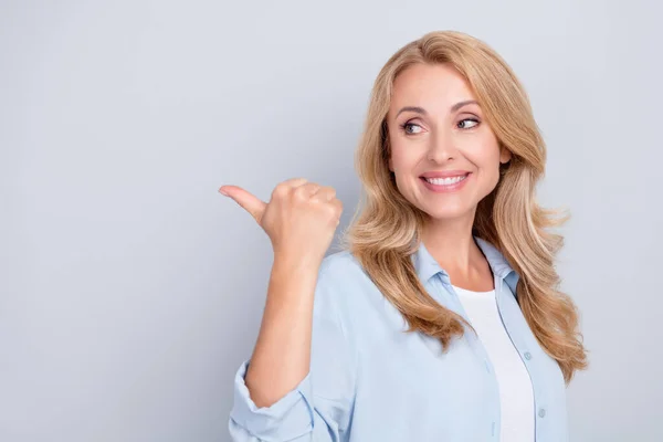 Foto de señora alegre mirar hacia otro lado del pulgar directo espacio vacío usar camisa azul aislado gris color fondo — Foto de Stock