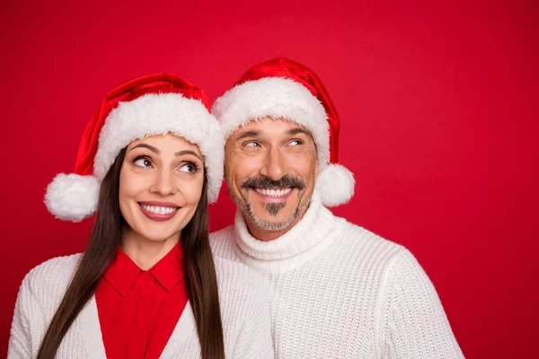 Photo de heureux mari joyeux femme couple porter santa chapeau regarder vide espace Noël isolé sur fond de couleur rouge — Photo