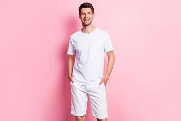 Retrato de atractivo chico alegre con ropa blanca cogido de la mano en bolsillos posando aislado sobre fondo de color pastel rosa —  Fotos de Stock