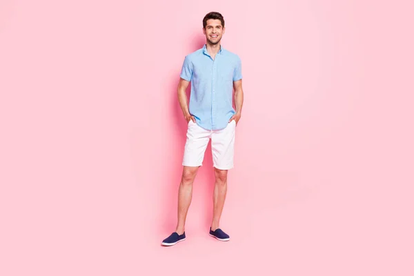 Foto de alegre guapo confiado chico manos bolsillos usar azul camisa pantalones cortos calzado aislado en color rosa fondo —  Fotos de Stock