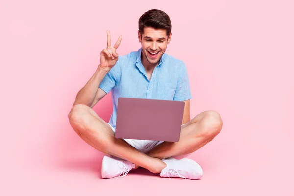 Foto de chico positivo hacer videollamada programa de computadora v-signo de desgaste camisa azul aislado en el fondo de color rosa —  Fotos de Stock