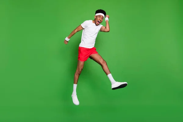 In voller Länge Foto von glücklichen funky dunkelhäutigen Kerl gekleidet Sport-Outfit springen hoch steigen Fäuste isoliert grüne Farbe Hintergrund — Stockfoto