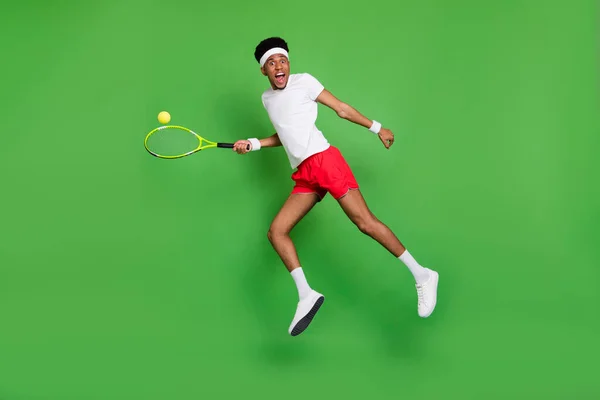 Lunghezza completa foto di abbastanza scioccato ragazzo pelle scura vestito abbigliamento sportivo giocare a tennis salto isolato colore verde sfondo — Foto Stock