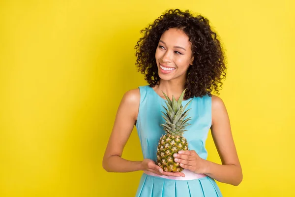 Photo de joyeux jeune femme heureuse peau sombre regarder vide espace tenir ananas isolé sur fond de couleur jaune — Photo