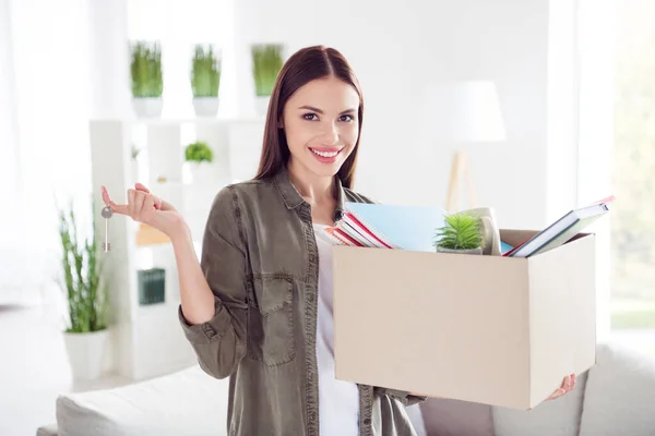 Foto de alegre linda mujer joven vestida camisa verde sosteniendo caja de papel nuevas llaves del apartamento interior casa casa habitación — Foto de Stock