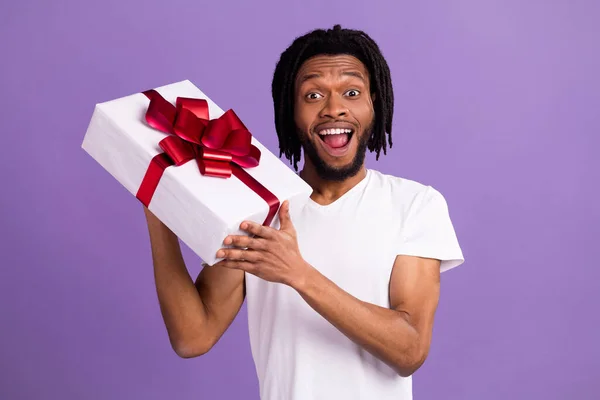 Portrait of attractive cheerful guy holding giftbox event congrats isolated over bright violet purple color background — Stock Photo, Image