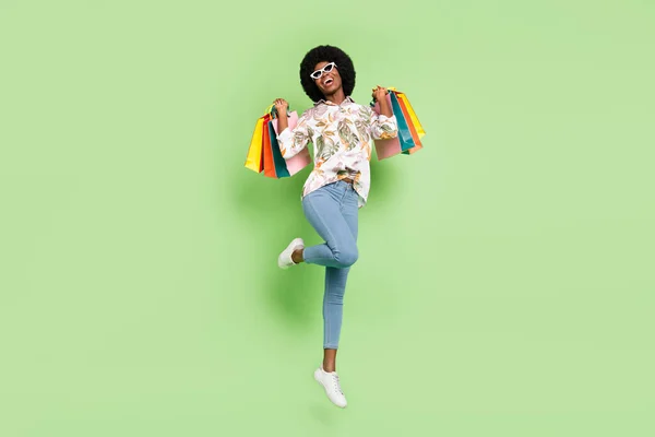 Foto de comprimento total de jovem menina preta feliz sorriso positivo salto segurar sacos shopaholic isolado sobre fundo de cor verde — Fotografia de Stock
