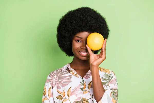 Foto de jovem atraente menina africana feliz sorriso positivo tampa olho laranja fruta isolada sobre fundo de cor verde — Fotografia de Stock