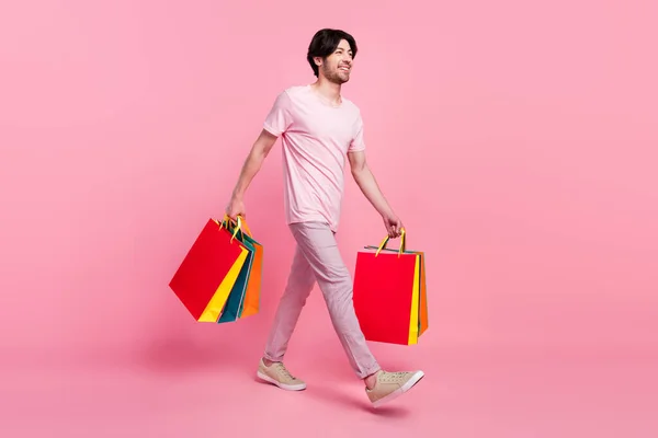 Full kropp profil sida foto av ung man glad positiv leende gå promenad hålla shoppingpåsar isolerade över rosa färg bakgrund — Stockfoto