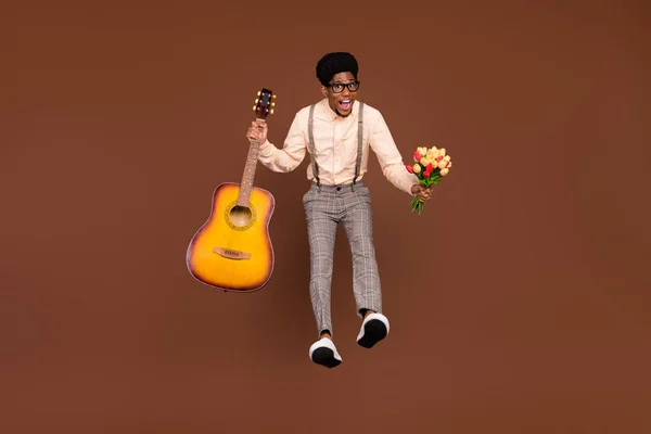 Foto de novio divertido chico salto celebrar guitarra ramo flores desgaste tirantes aislado color marrón fondo — Foto de Stock