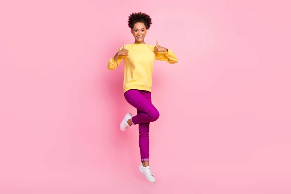Fotografie atraktivní hezká dáma nosit žlutý svetr skákání vysoko ukazující palce nahoru usmívající se izolované růžové barvy pozadí — Stock fotografie