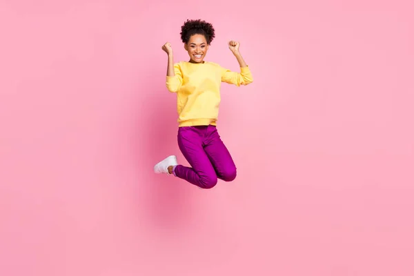 Foto van glanzende mooie vrouw gekleed gele trui glimlachen springen hoog stijgende vuisten geïsoleerde roze kleur achtergrond — Stockfoto